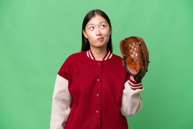 Joven asiática con guante de béisbol sobre un fondo aislado y mirando hacia arriba