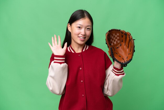 Joven asiática con guante de béisbol sobre un fondo aislado saludando con la mano con expresión feliz