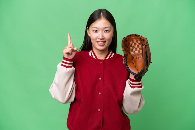 Joven asiática con guante de béisbol sobre un fondo aislado señalando una gran idea