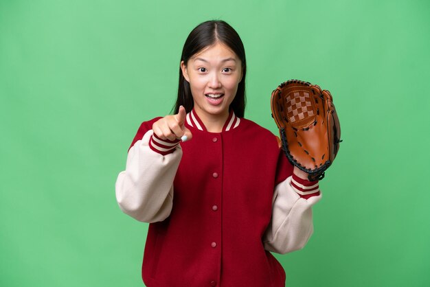 Joven asiática con guante de béisbol sobre un fondo aislado sorprendida y apuntando al frente