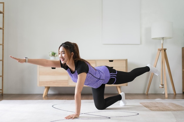 Joven asiática haciendo ejercicio de equilibrio de yoga con pose de perro pájaro para un estilo de vida saludable en casa