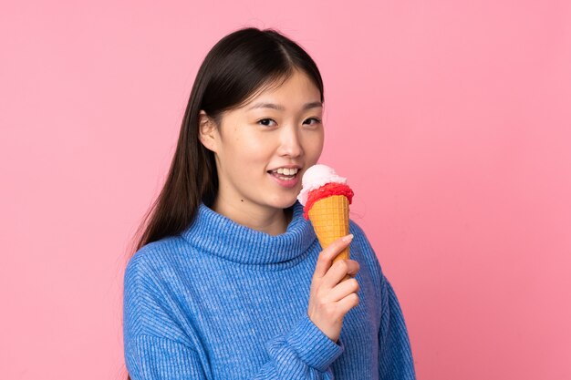 Joven asiática con un helado de cucurucho en pared rosa