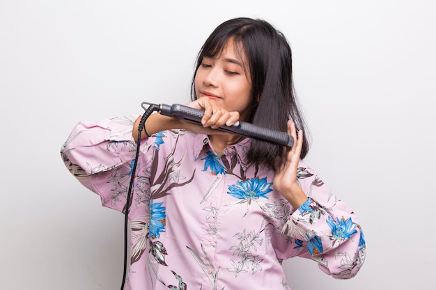 Joven asiática hermosa mujer feliz alisar el cabello con plancha de pelo sobre fondo blanco.