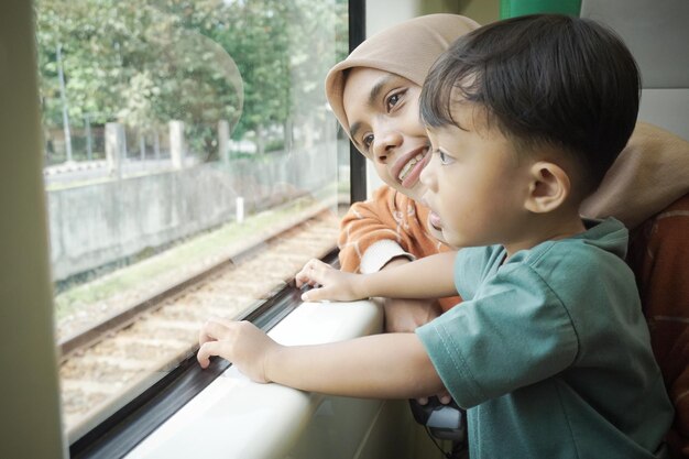 Una joven asiática con hiyab y su hijo están hablando y mirando por la ventana dentro del tren