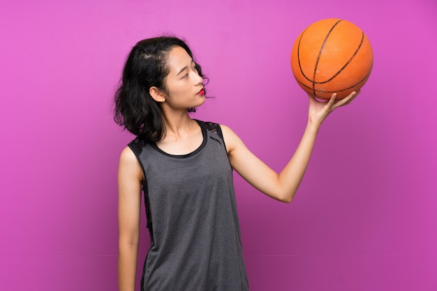 Joven asiática jugando baloncesto sobre fondo púrpura aislado