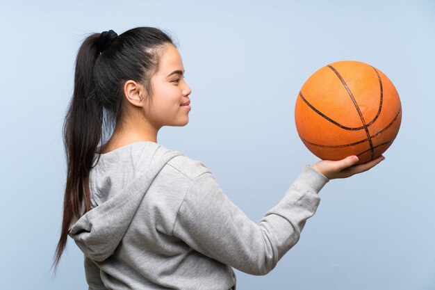 Joven asiática jugando baloncesto sobre pared aislada