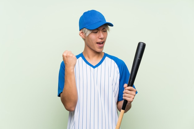 Joven asiática jugando béisbol sobre verde aislado celebrando una victoria