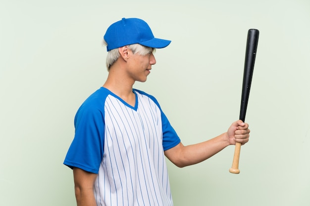 Joven asiática jugando béisbol sobre verde aislado con expresión feliz