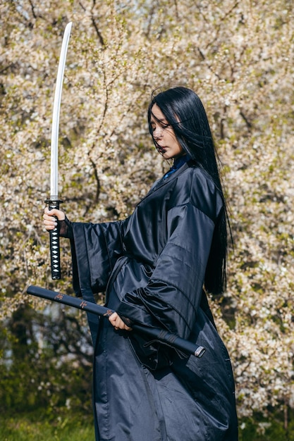 Foto joven asiática en kimono negro tradicional con espada contra el fondo de la naturaleza