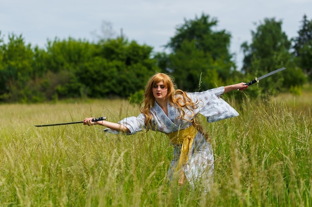 Joven asiática en kimono tradicional entrena técnicas de lucha con espada katana al aire libre, chica guerrera samurai