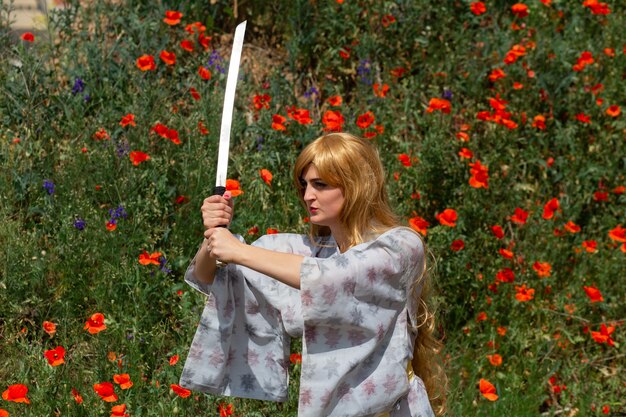 Joven asiática en kimono tradicional entrena técnicas de lucha con espada katana en las colinas con amapolas rojas, chica guerrera samurai