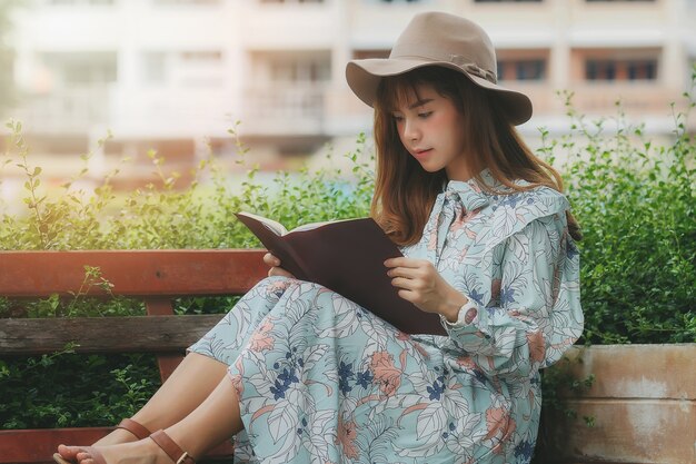 Joven asiática leyendo un libro en el banco en el parque