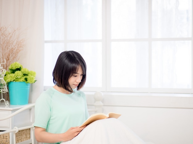 Joven asiática leyendo un libro en la cama