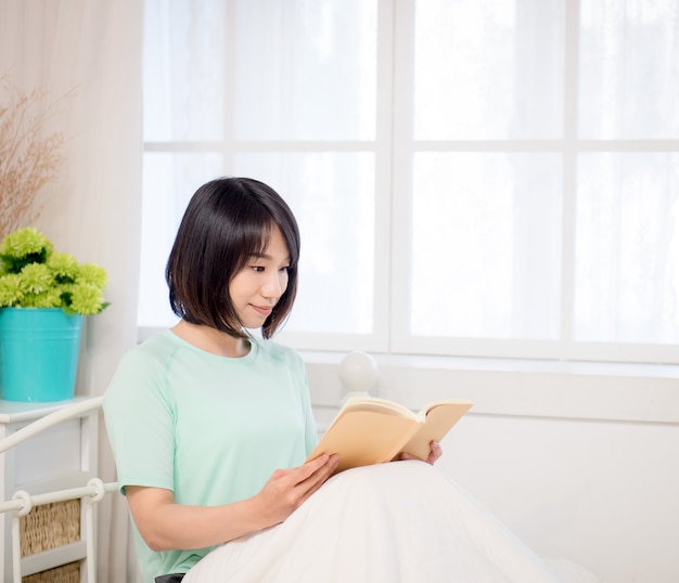 Joven asiática leyendo un libro en la cama