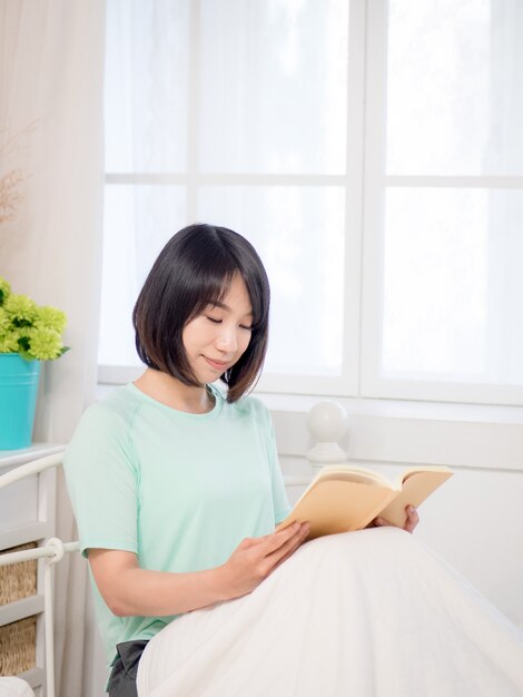 Joven asiática leyendo un libro en la cama