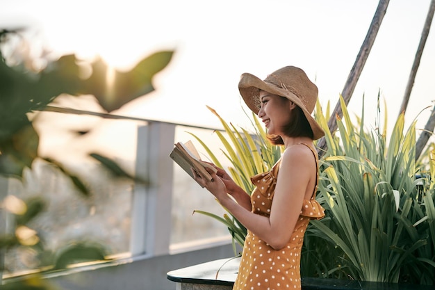 Joven asiática leyendo en la naturaleza bajo el sol de verano