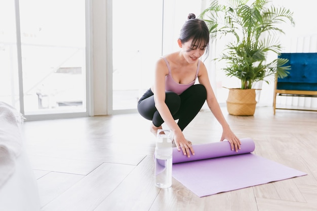 Joven asiática manos rodando colchoneta de yoga con botella de agua preparándose para hacer yoga Trabajando en casa o en un estudio de yoga Hábitos saludables para mantenerse en forma conceptos de pérdida de peso