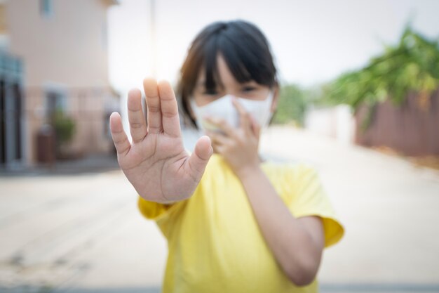 Joven asiática con máscara para proteger covid 19, niño tailandés usar máscara antipolvo. para proteger pm2.5 y mostrar el gesto de detener las manos para detener el brote del virus corona.