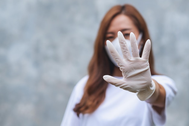 Una joven asiática con mascarilla protectora y guantes médicos de goma que muestra el signo de la mano para la atención médica y el concepto Covid19
