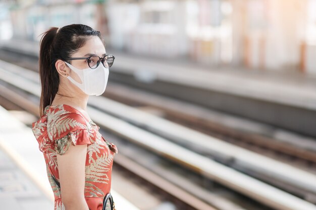 Joven asiática con mascarilla quirúrgica proteger la inflexión de coronavirus en la estación de tren público