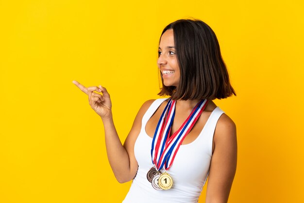 Joven asiática con medallas aislado en la pared blanca apuntando con el dedo hacia un lado y presentando un producto