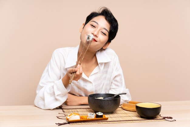 Joven asiática en una mesa con tazón de fideos y sushi