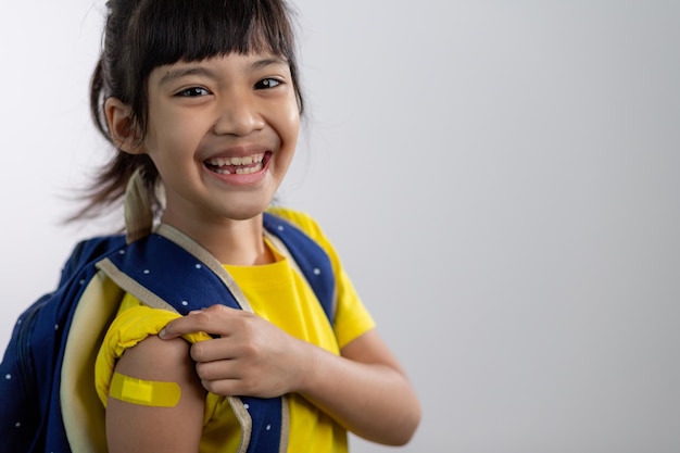 Joven asiática mostrando su brazo con vendaje amarillo después de vacunarse o inocularse, inmunización infantil, concepto de vacuna covid delta