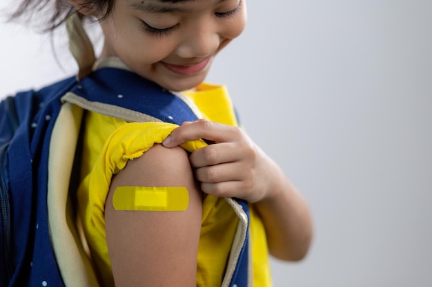 Joven asiática mostrando su brazo con vendaje amarillo después de vacunarse o inocularse, inmunización infantil, concepto de vacuna covid delta