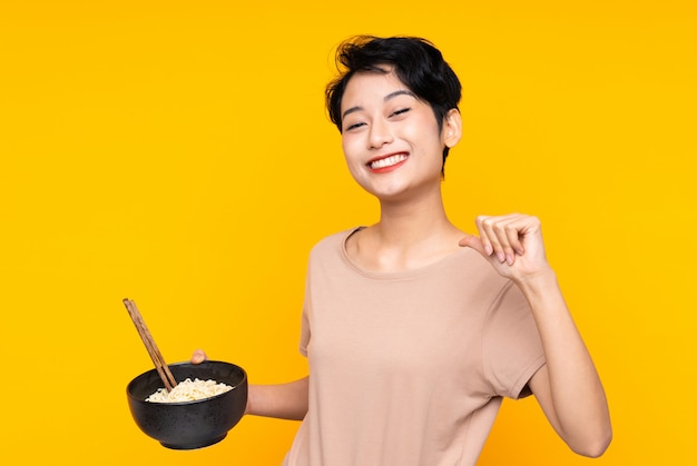 Joven asiática orgullosa y satisfecha mientras sostiene un plato de fideos con palillos