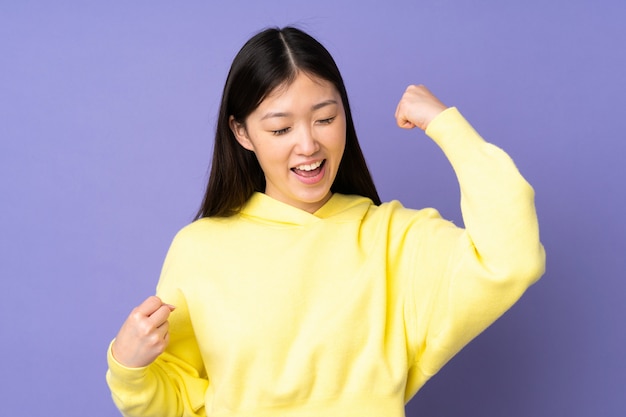 Joven asiática en pared púrpura celebrando una victoria