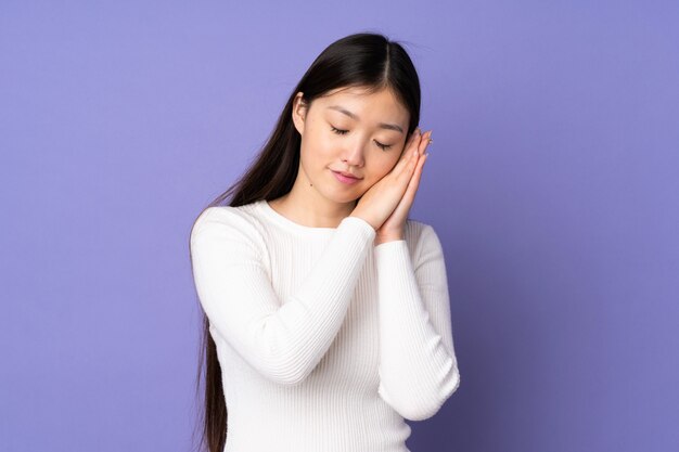 Joven asiática en pared púrpura haciendo gesto de sueño en expresión dorable