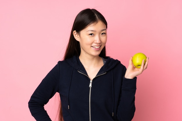 Joven asiática en pared rosa con una manzana y feliz