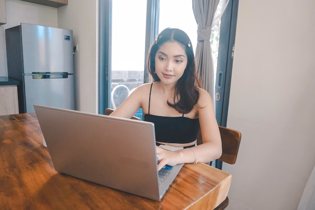 Una joven asiática pasa su tiempo en casa sentada en el comedor trabajando en su laptop