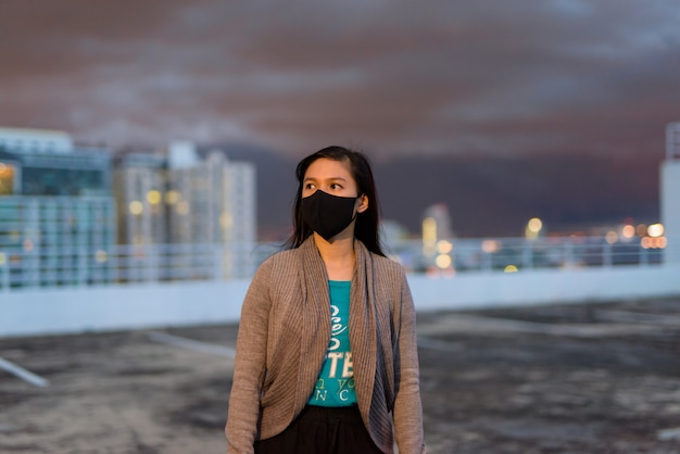 Joven asiática pensando con máscara para protegerse del brote del virus corona durante el clima tempestuoso al aire libre