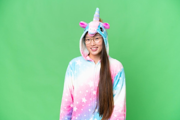 Joven asiática con pijama de unicornio sobre un fondo aislado de clave de croma con gafas y feliz