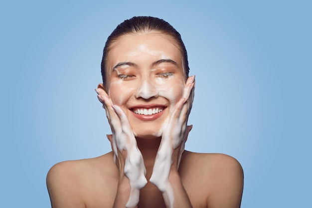 Foto joven asiática que aplica uso de espuma de lavado facial de cerca en azul aislado cuidado de la piel mujeres belleza