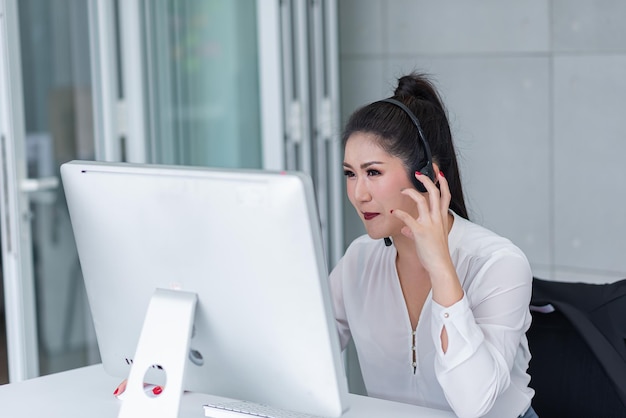 joven asiática que trabaja recibiendo llamadas usando auriculares consultando o resolviendo problemas