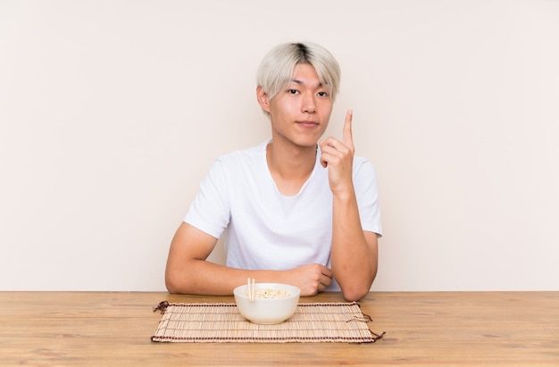 Joven asiática con ramen en una mesa señalando con el dedo índice una gran idea