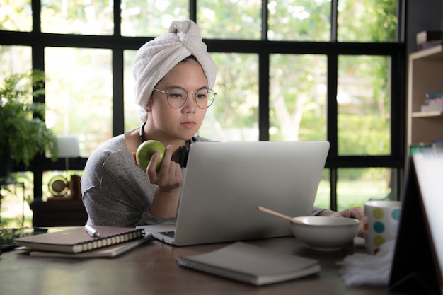 Joven asiática en ropa casual usando laptop y sonriendo mientras trabaja desde casa