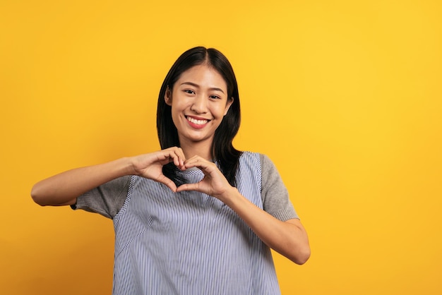 Joven asiática con ropa informal sonriendo y usando las manos para hacer publicidad con fondo amarillo