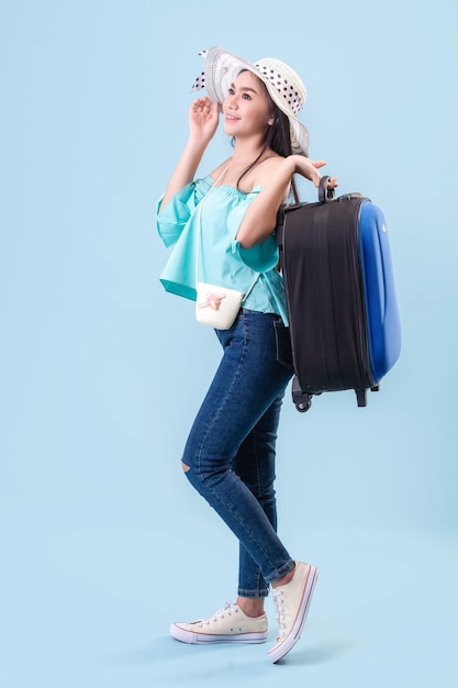 Una joven asiática de rostro brillante, con sombrero. Celebración de equipaje para viajar en verano en estudio Fondo azul pastel. Filtros de tono azul pastel.