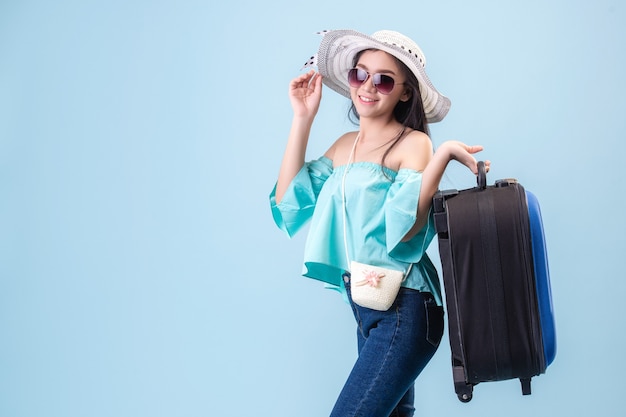 Foto una joven asiática de rostro brillante, con sombrero y gafas. con equipaje para viajar en verano en estudio fondo azul pastel. filtros de tono azul pastel.