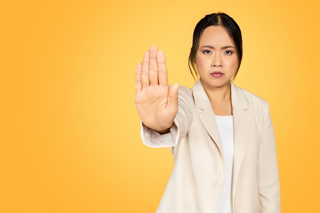 Una joven asiática segura y enojada en traje hace un gesto de parada con la mano.