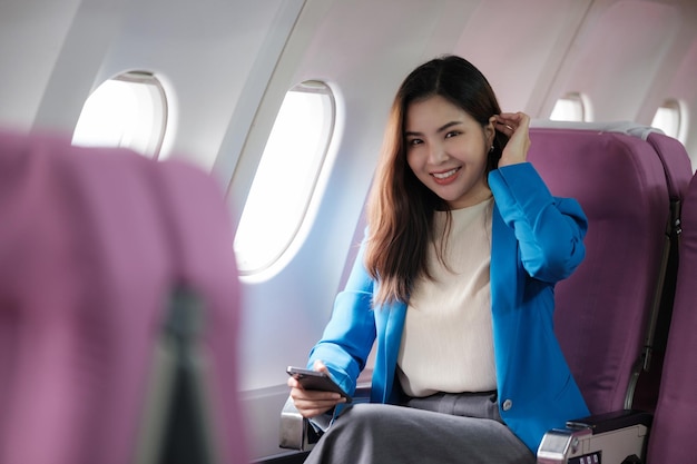 Una joven asiática sentada en el asiento del avión y hablando por teléfono inteligente Una joven viajera hablando por teléfono celular