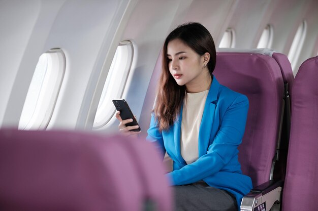 Foto una joven asiática sentada en el asiento del avión y hablando por teléfono inteligente una joven viajera hablando por teléfono celular