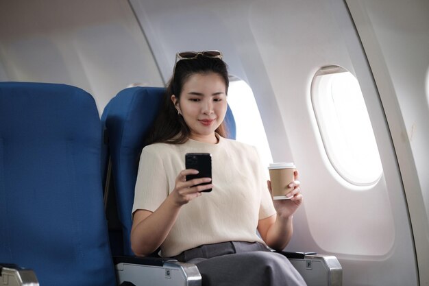 Una joven asiática sentada en el asiento del avión y hablando por teléfono inteligente Una joven viajera hablando por teléfono celular