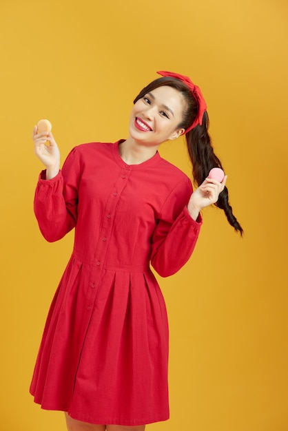 Joven asiática sobre fondo amarillo aislado sosteniendo coloridos macarons franceses