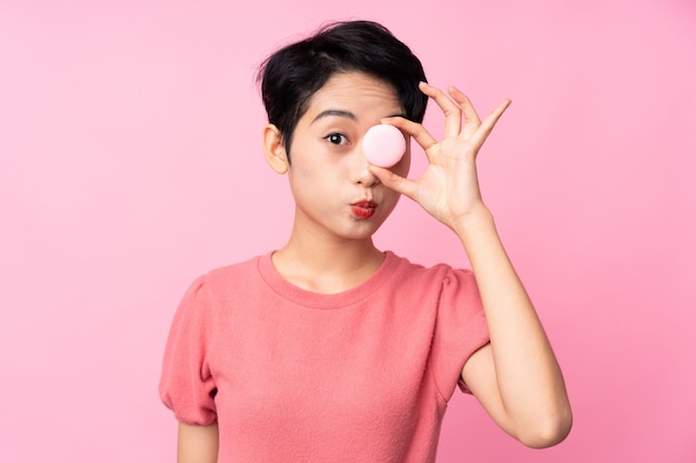Joven asiática sobre pared rosa aislada con coloridos macarons franceses con cara divertida