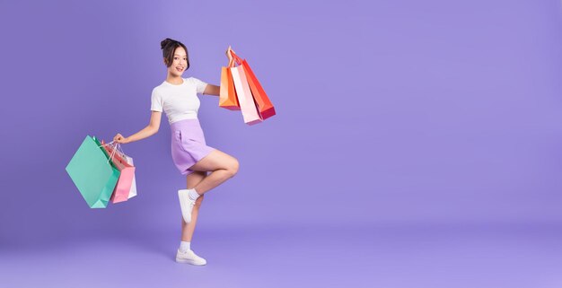 Joven asiática sosteniendo una bolsa de compras sobre fondo púrpura