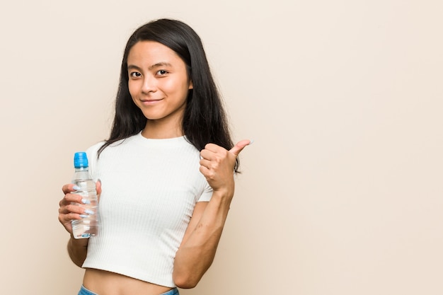 Joven asiática sosteniendo una botella de agua sonriendo y levantando el pulgar